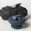 Decorative stone bowl with crystals, bottle of精油, and rock on a light background