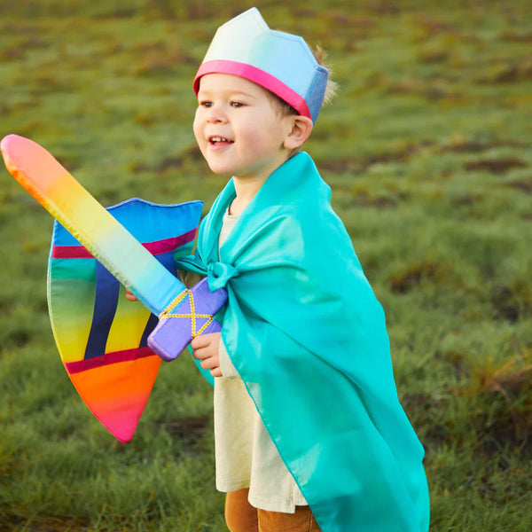 Child in a costume holding a colorful sword and shield outdoors.