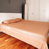 Bed with beige sheets and pillow in a room with wooden floor and white walls.