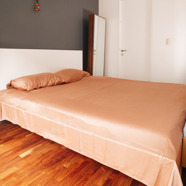Bed with beige sheets and pillow in a room with wooden floor and white walls.