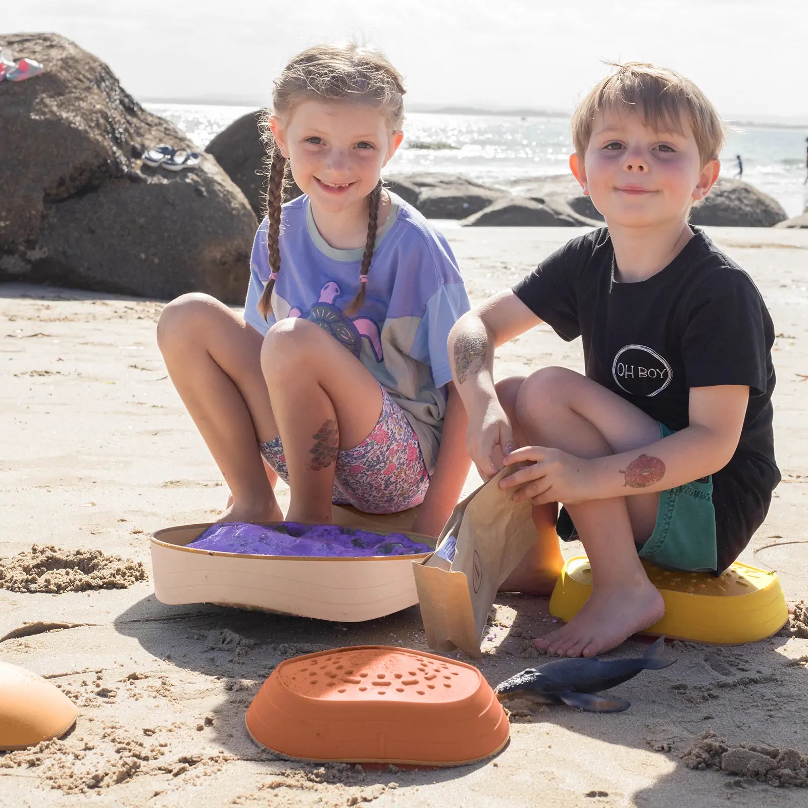 Two children sitting on beach toys at the beach.