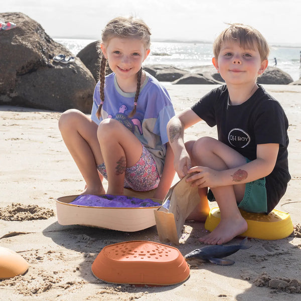 Two children sitting on beach toys at the beach.