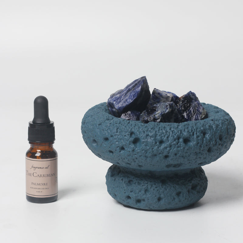 Blue volcanic ash bowl with dark stones and a bottle of essential oil on a white background