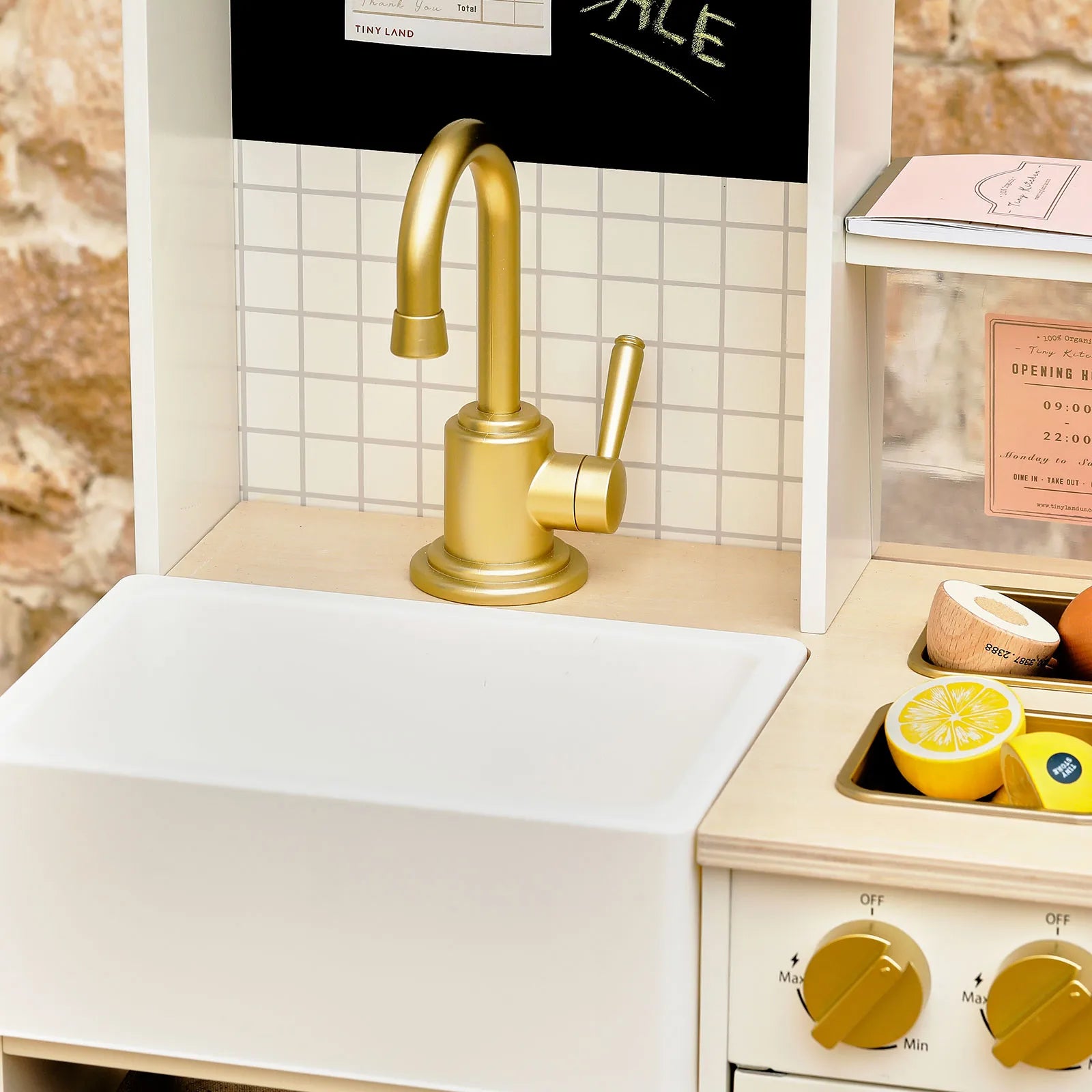 Gold kitchen faucet over a white sink with a small stove and lemon on a countertop.