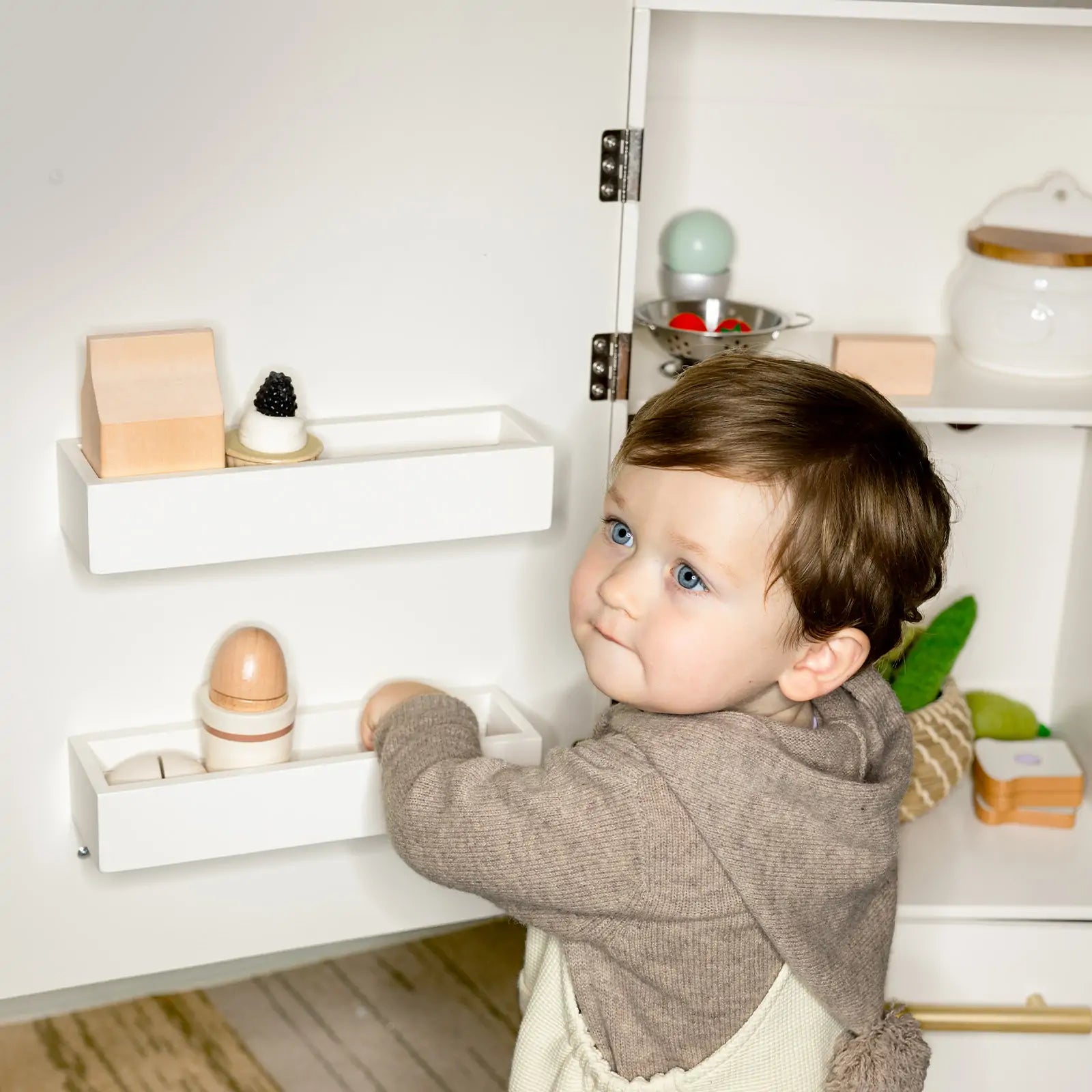 Child playing with wooden toys on a shelf in a minimalistic room.