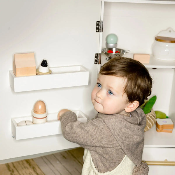 Child playing with wooden toys on a shelf in a minimalistic room.