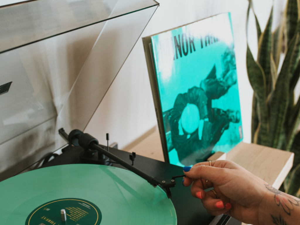 Person placing a green vinyl record into a turntable with a blurred background