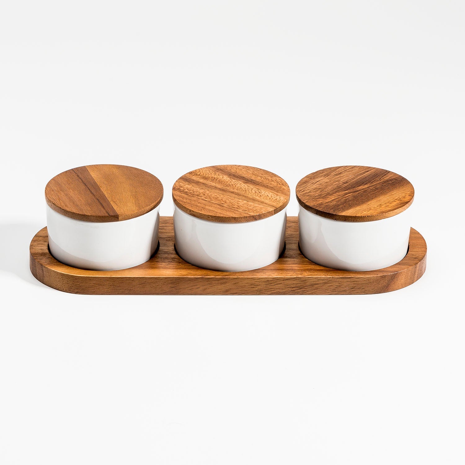 Three white jars with wooden lids on a wooden tray against a white background