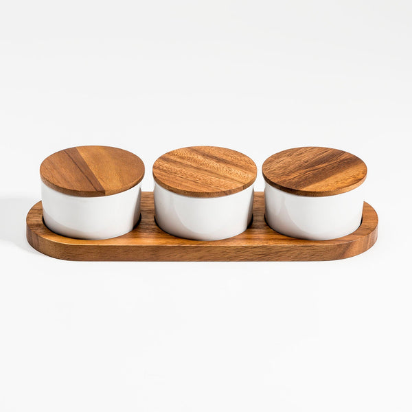 Three white jars with wooden lids on a wooden tray against a white background