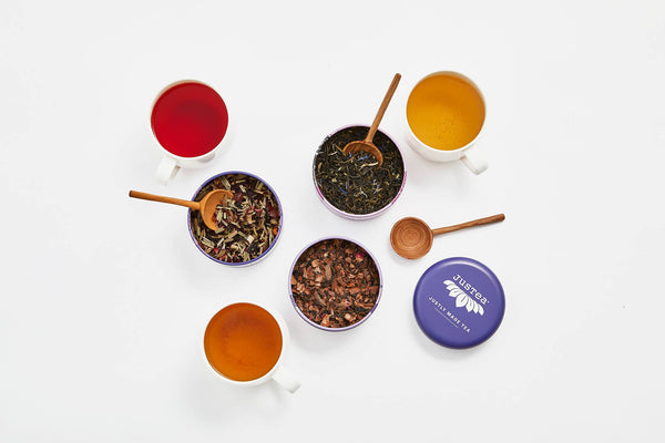 Assorted teas in cups and bowls with a purple tin labeled 'Teavana' on a white background.