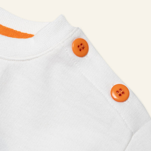 Close-up of a white garment with orange buttons on a light background