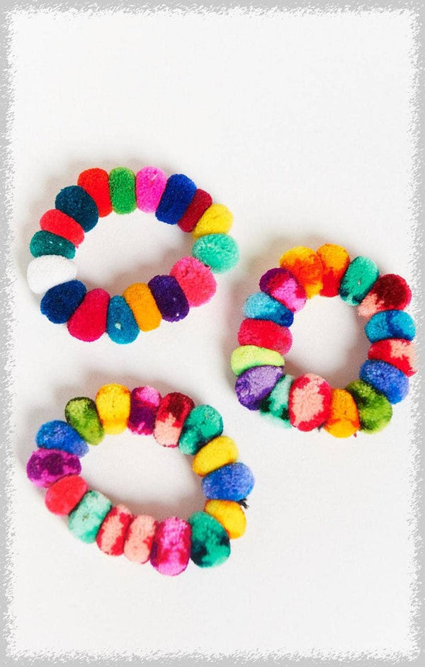Three colorful pom-pom hair ties on a white background. Add a pop of color with our handmade Pom Pom Hair Tie Scrunchies from Peru! Fun, durable, and eco-friendly, these multicolored accessories double as hair ties or bracelets. Perfect for gifts, boutiques, or everyday style.
