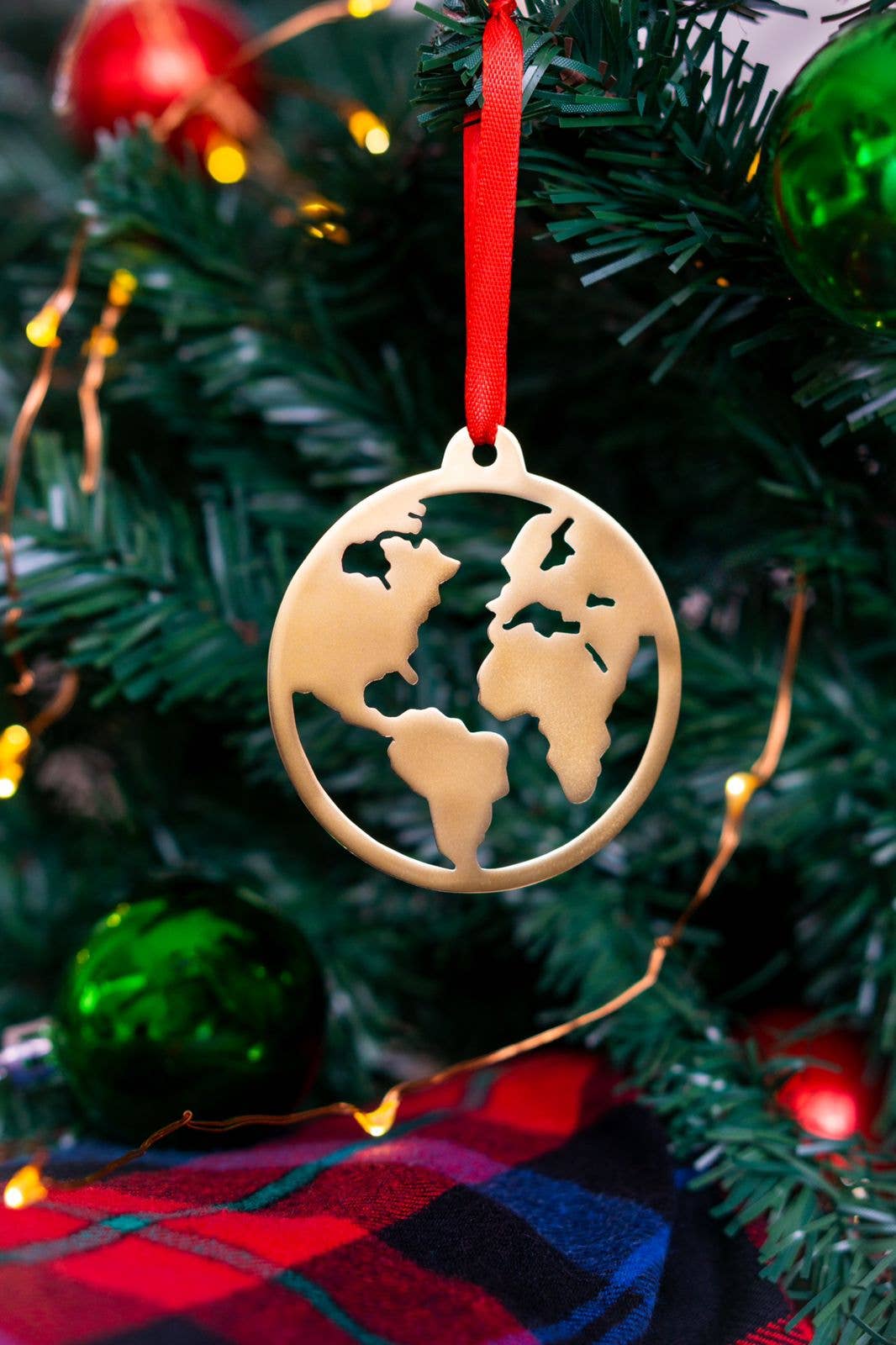 Gold world map ornament on a Christmas tree with red and green decorations.