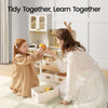 A woman and a young girl play with a wooden toy kitchen set in a bright room. The scene includes white storage bins, toy fruit, and the text 'Tidy Together, Learn Together' at the top.