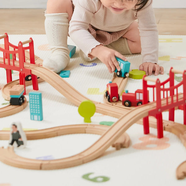 Child playing with a wooden train set on a white surface