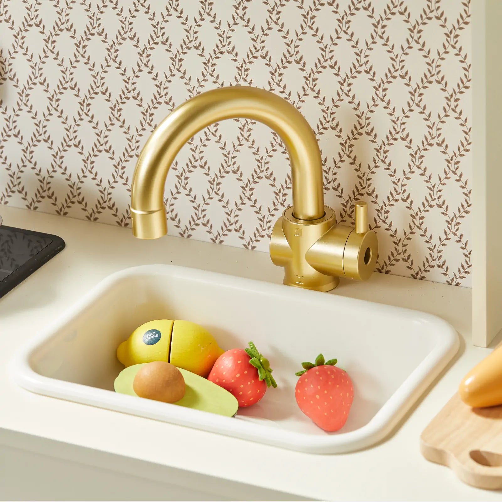 Children's toy kitchen set with a gold faucet and sink against a patterned wall.
