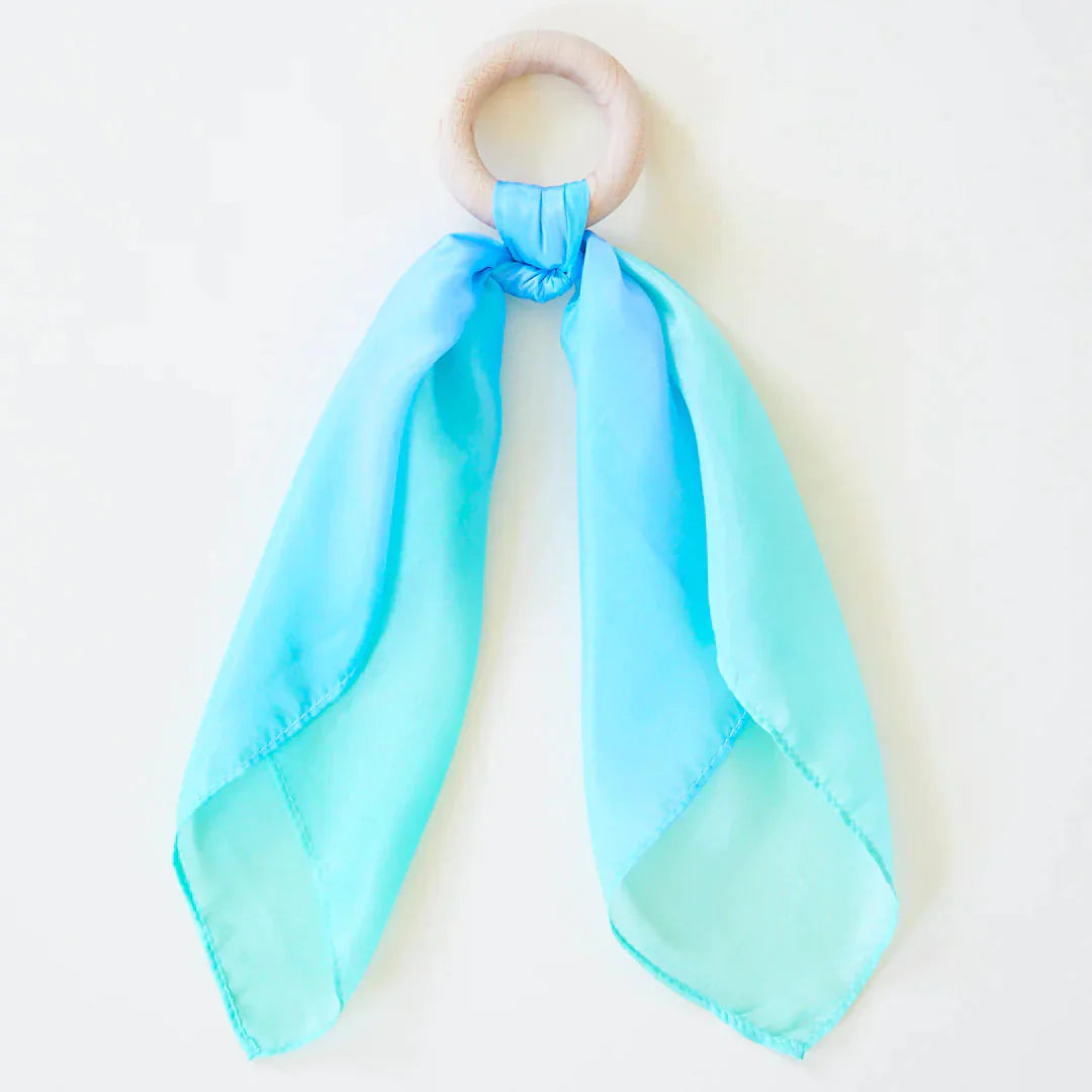 Baby holding the Sarah's Silks Sea Teether maple wood ring with flowing sea-coloured playsilk