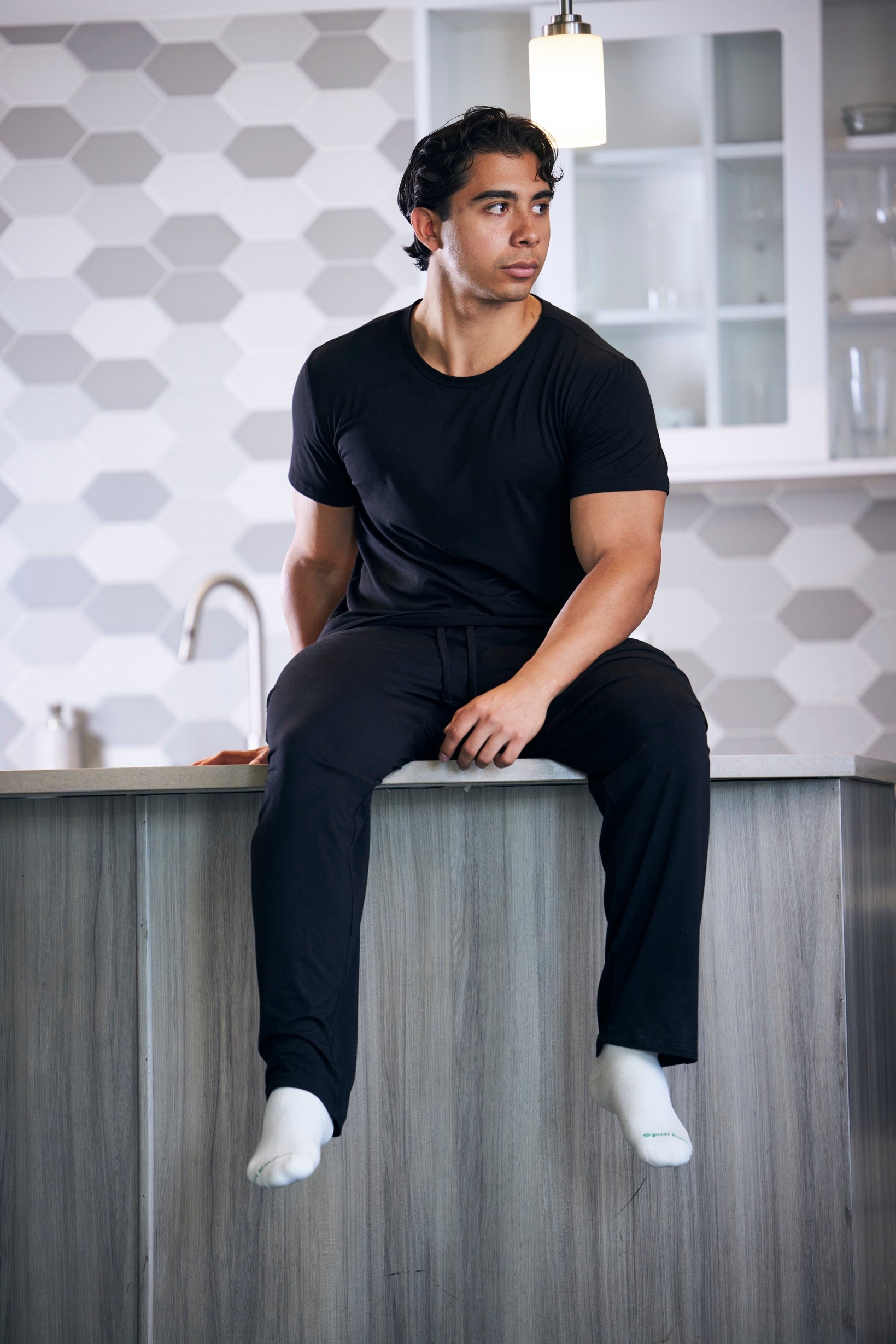 Man sitting on a kitchen counter wearing black clothing.