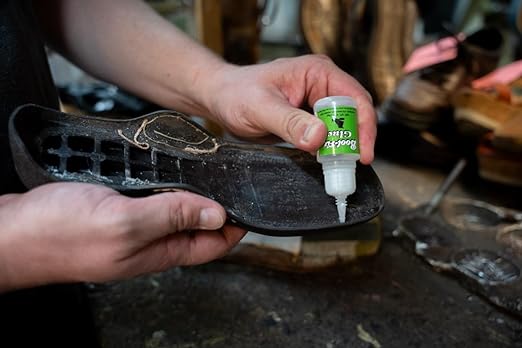 Person applying a green bottle of shoe polish to a black shoe in a workshop setting.