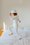 Person in white pajamas and towel on head standing on a bed.