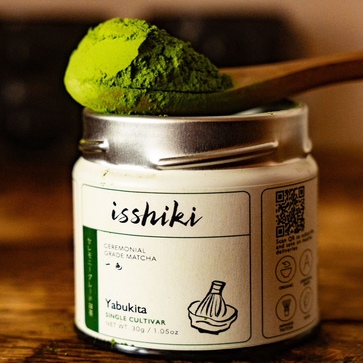 Jar of isshiki Yabukita matcha with a scoop of green powder on a wooden surface.