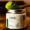 Jar of isshiki Yabukita matcha with a scoop of green powder on a wooden surface.
