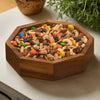 Wooden bowl filled with a mix of nuts and colorful candies on a light surface.