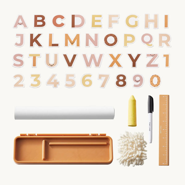 A children's alphabet and number craft kit laid out on a light cream background. The set includes decorative alphabet letters A through Z and the numbers 0 through 9 in soft pastel and earthy tones, a white roll of paper, a yellow cone, a black-and-white marker, a wooden ruler, a small orange tray, and a white textured sponge.