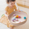 Child playing with colorful balls in a bowl on a light wooden floor.