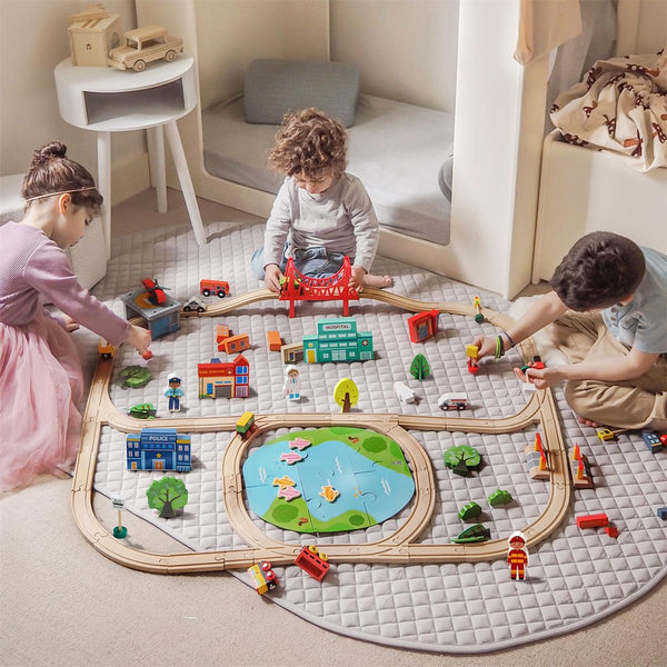 Children playing with a toy train set on a mat in a room.
