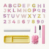 A children's alphabet and number learning set arranged on a light cream background, including pastel alphabet letters, numbers 0-9, a yellow tray, a white roll, a pink crayon, a white marker, and a pink microfiber brush.