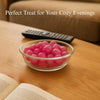 Glass bowl of pink gumballs on a wooden table with a remote control and book, text 'Perfect Treat for Your Cozy Evenings'.