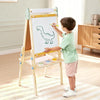 Child drawing a dinosaur on a whiteboard with a yellow marker, standing in a room with wooden furniture.