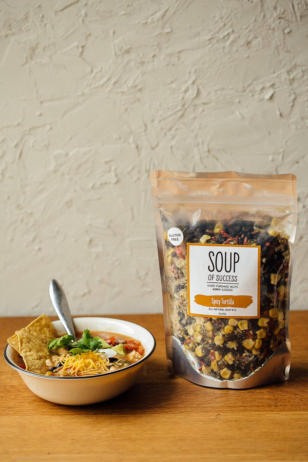 Bag of Soup of Success mix next to a bowl of soup on a wooden surface.
