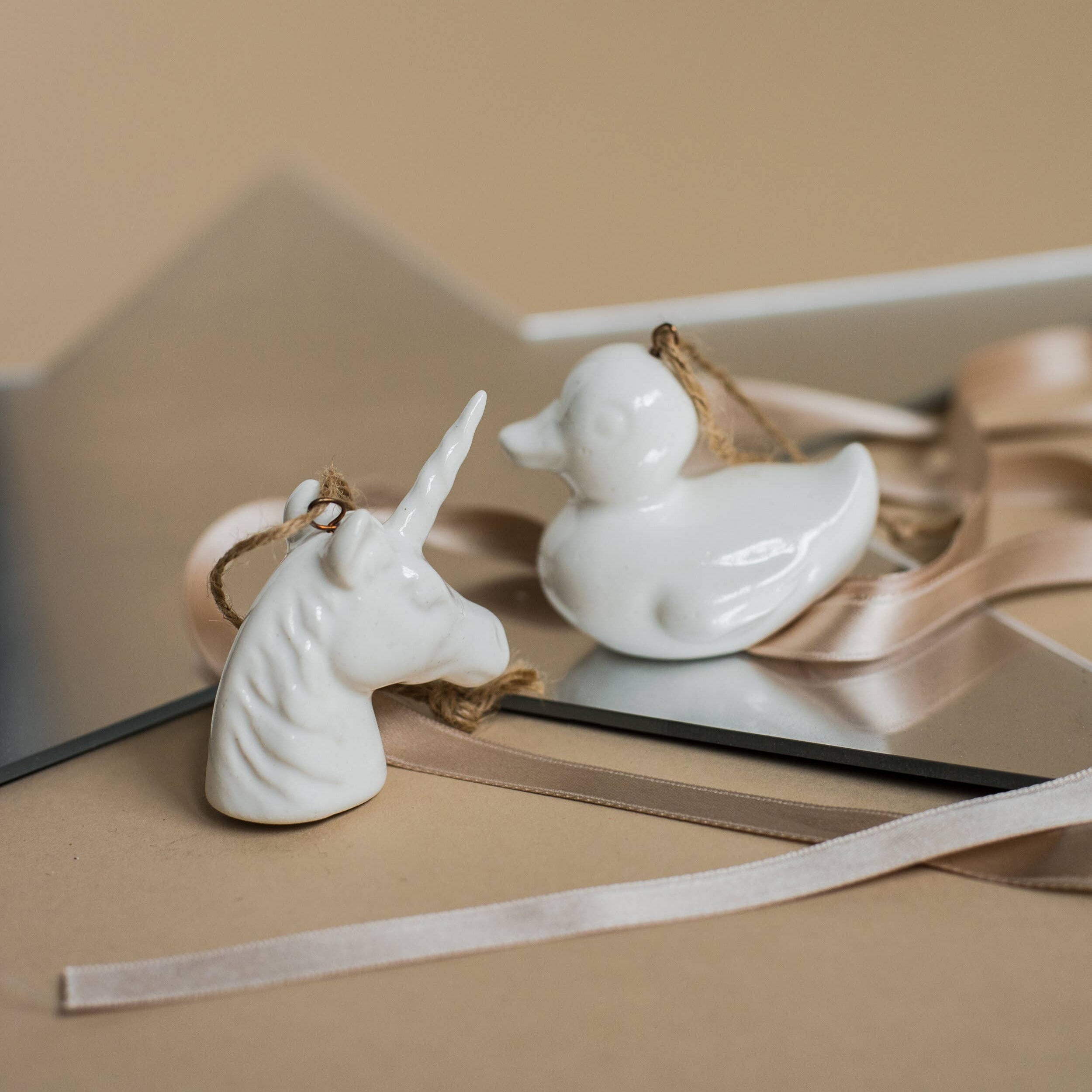 White ceramic unicorn and duck figurines on a reflective surface with a neutral background
