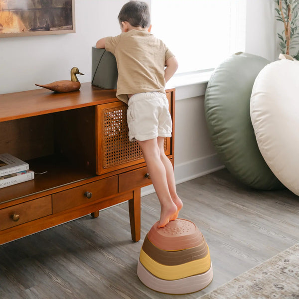 Child standing on a colorful step stool in a living room.