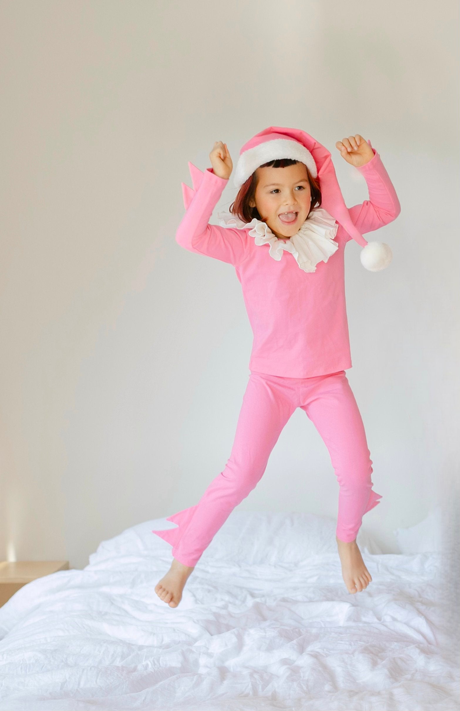 Child in pink pajamas and Santa hat jumping on a bed