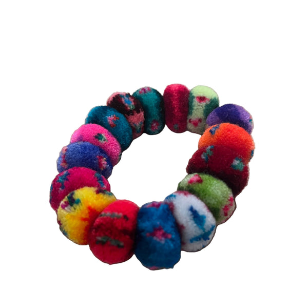 Colorful pom-pom hair tie on a wooden surface