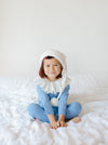 Child wearing a blue outfit with a white hood sitting on a white bed.