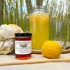 Jar of Miombo Blossom Honey with a glass of orange juice and lemon on a wooden surface with a natural background.