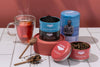 Tea tins with tea leaves and a glass of tea on a tiled surface.