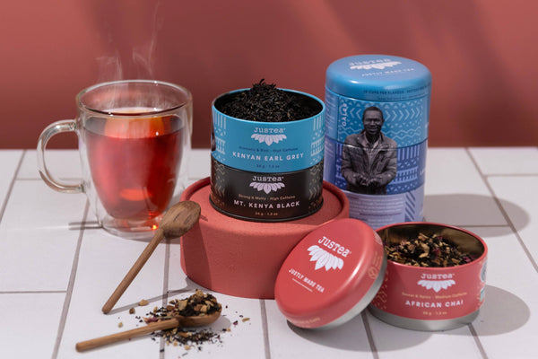 Tea tins with tea leaves and a glass of tea on a tiled surface.