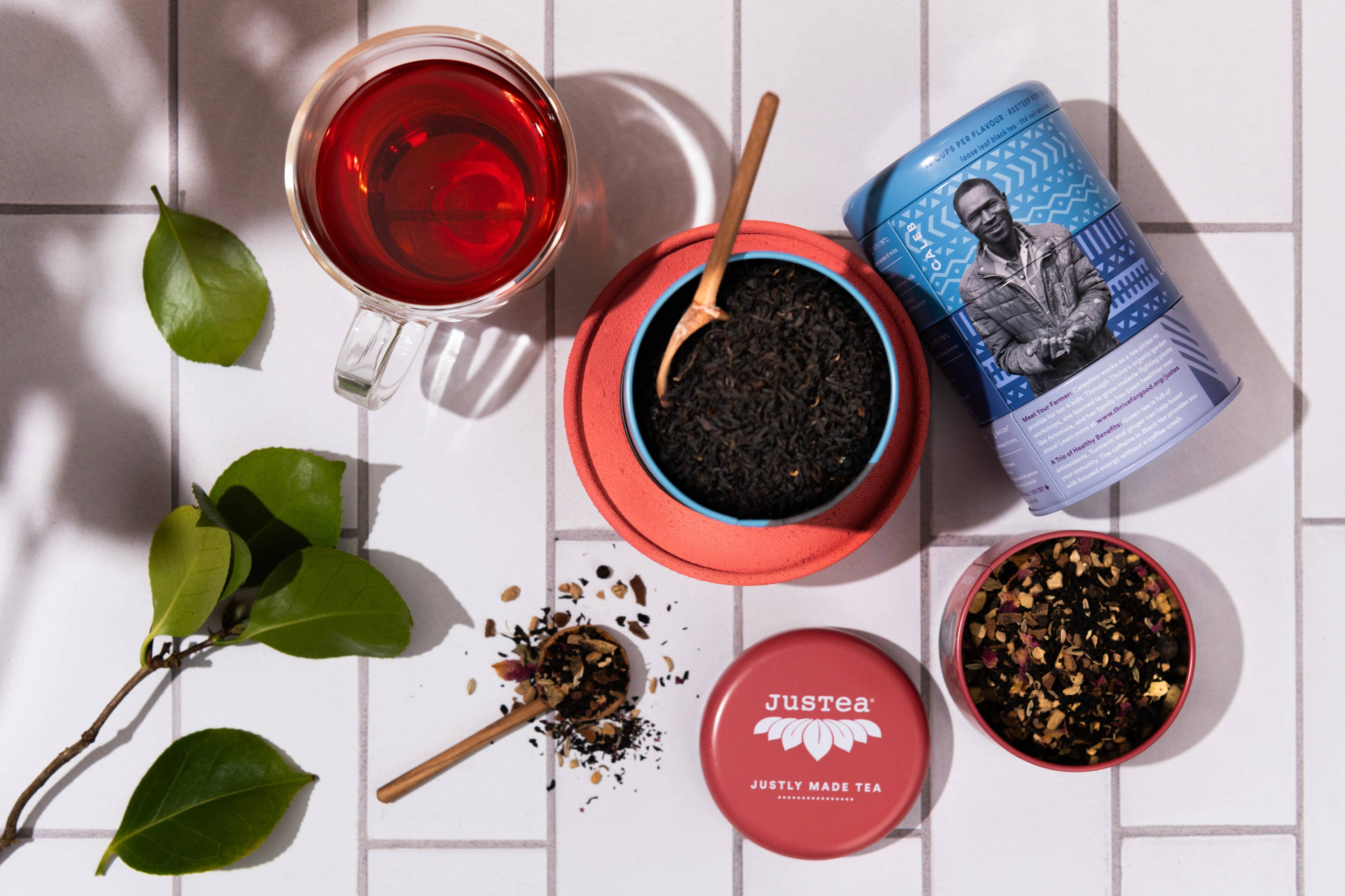 Tea-making setup with a mug of red tea, loose tea leaves, and Justea containers on a white surface.