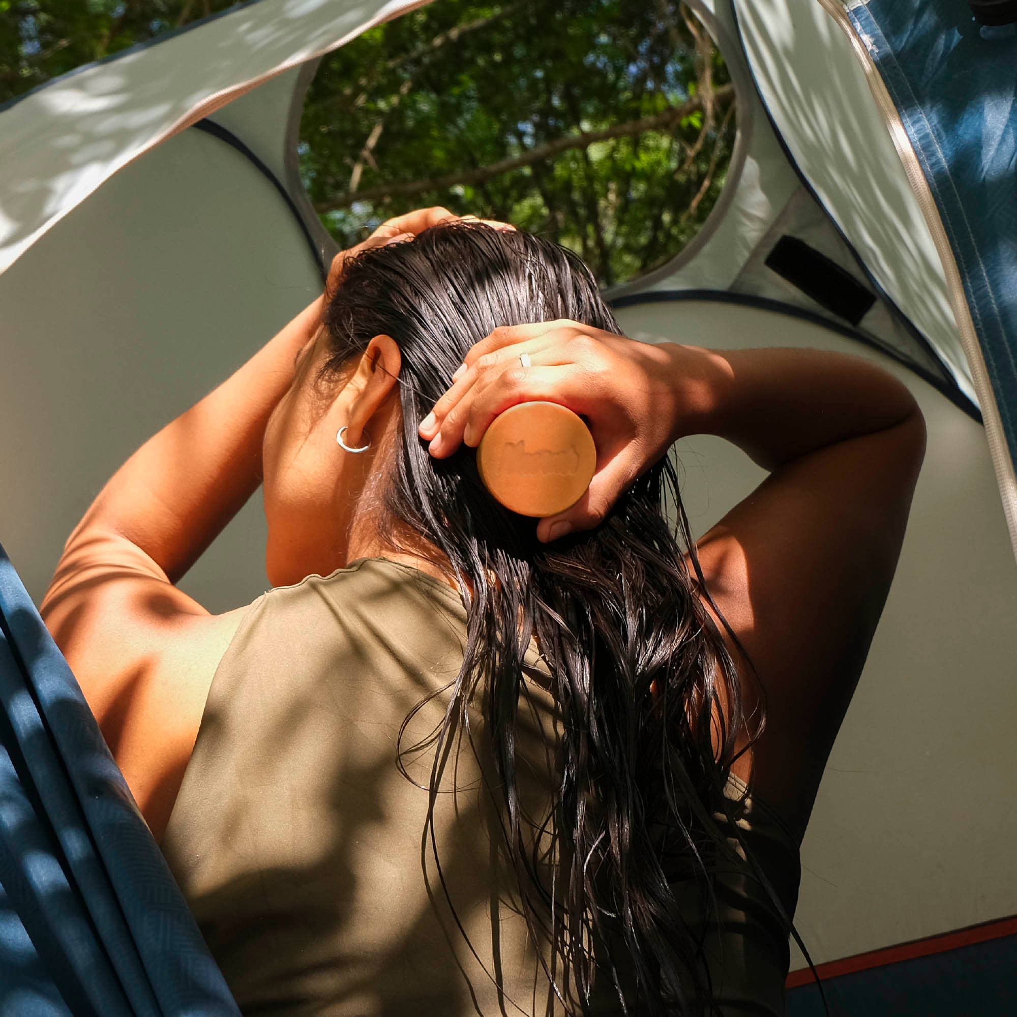 Person with wet hair using a hairbrush inside a vehicle. NANAH Curly Hair conditioner bar — sulfate-free, defines & hydrates curls with vegetable keratin, castor oil & jojoba. Curly Girl Method approved. Shop now.