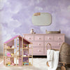 Dollhouse with furniture and accessories in a room with a pink dresser and decorative mirror.