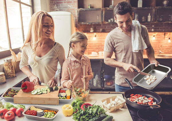 Family of three cooking together in a kitchen with various vegetables and cookware.