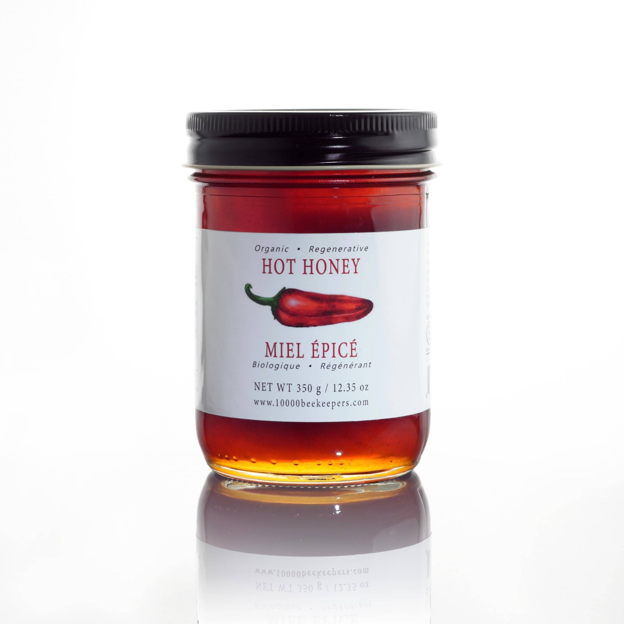 Jar of hot honey with a label featuring a red chili pepper on a white background. Spice up your meals with Organic Hot Honey – fair-trade, unpasteurized forest honey infused with Ontario chili peppers. Sweet, spicy, and sustainable. Perfect on pizza, cheese, or ice cream. Shop now!