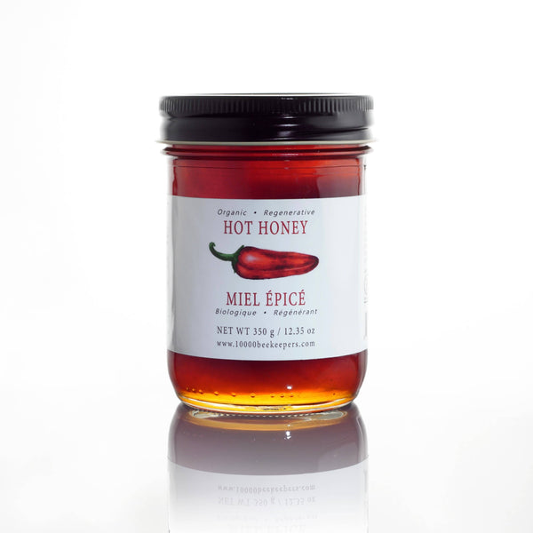 Jar of hot honey with a label featuring a red chili pepper on a white background. Spice up your meals with Organic Hot Honey – fair-trade, unpasteurized forest honey infused with Ontario chili peppers. Sweet, spicy, and sustainable. Perfect on pizza, cheese, or ice cream. Shop now!