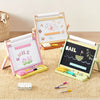 Three small children's magnetic drawing easels arranged on a beige rug. One easel is pink and white with a 'SMILE' board and tulips, one is light wood with alphabet letters, and one is black with a sailboat drawing.