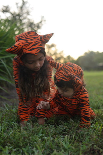 Two children in tiger-striped outfits playing on grass.
